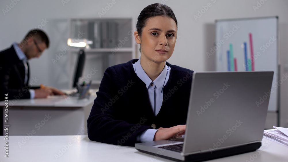 Female manager typing on laptop and smiling at camera, workday in big company Female manager typing on laptop and smiling at camera, workday in big company
