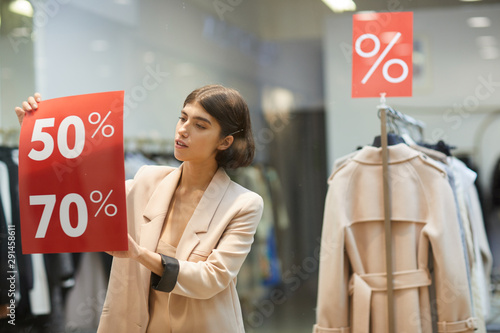 Quadro em tela Waist up portrait of beautiful woman hanging red SALE signs on window display in