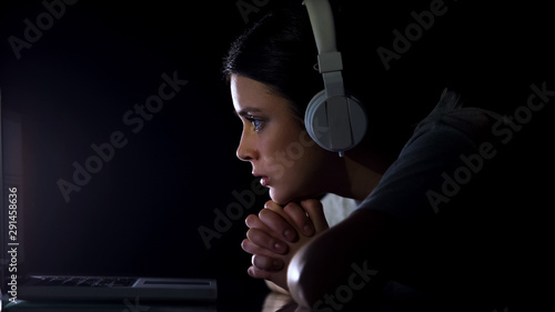 Worried woman in headset watching online movie at night, interesting film photo