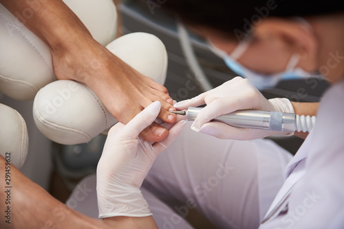 Pedicurist using electric nail drill while doing pedicure for young lady