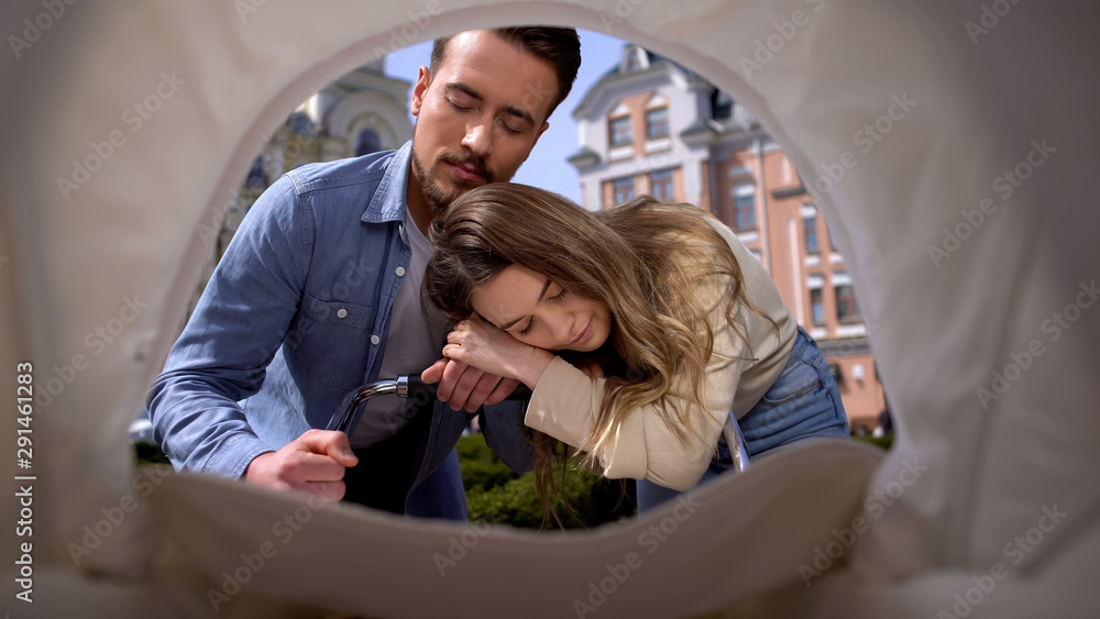 Tired mother and father falling asleep swinging baby pram, parenthood exhaustion Tired mother and father falling asleep swinging baby pram, parenthood exhaustion