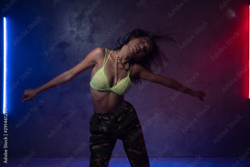 Young beautiful fashion Asian girl dancer wearing stylish clothes dancing in studio with neon lights