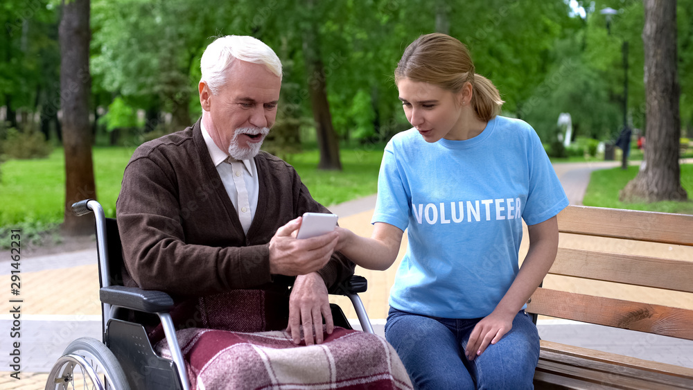 Female volunteer teaching handicapped man use smartphone, relaxing at park Female volunteer teaching handicapped man use smartphone, relaxing at park