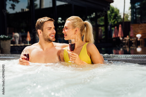 sexy couple holding glasses of red wine in swimming pool in sunny day