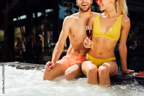 cropped view of sexy smiling couple with red wine and strawberries in swimming pool