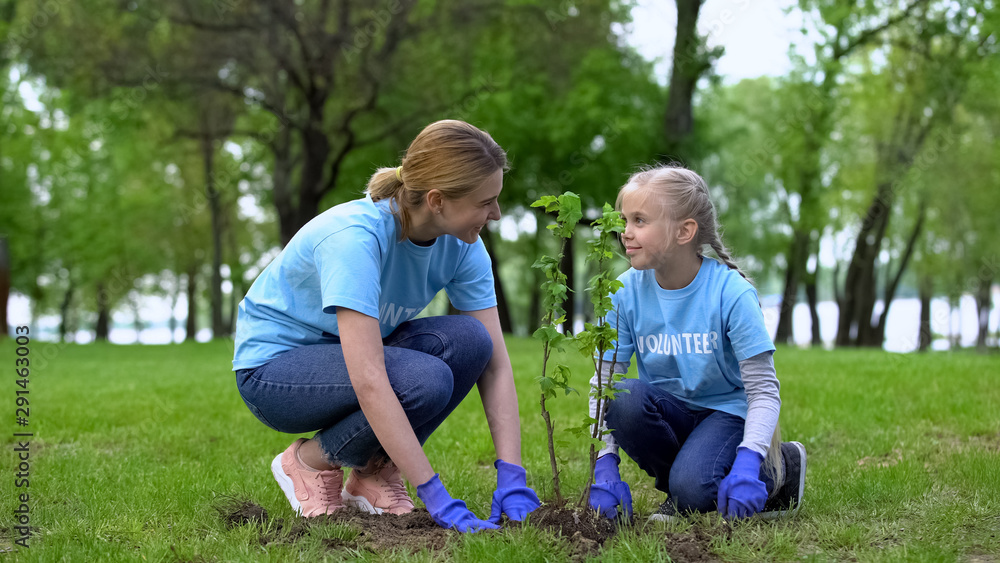 Mom and daughter planting tress in park together, eco volunteer work, earth care