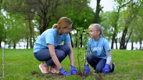 Mom and daughter planting tress in park together, eco volunteer work, earth care