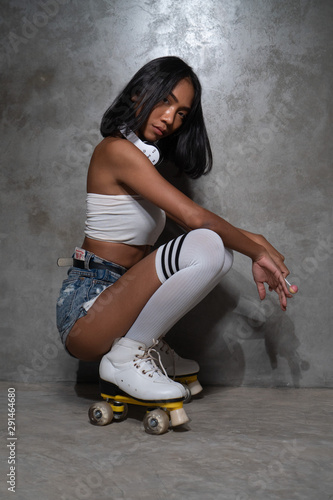 Young beautiful Asian girl in retro quads roller skates posing in studio over concrete wall background