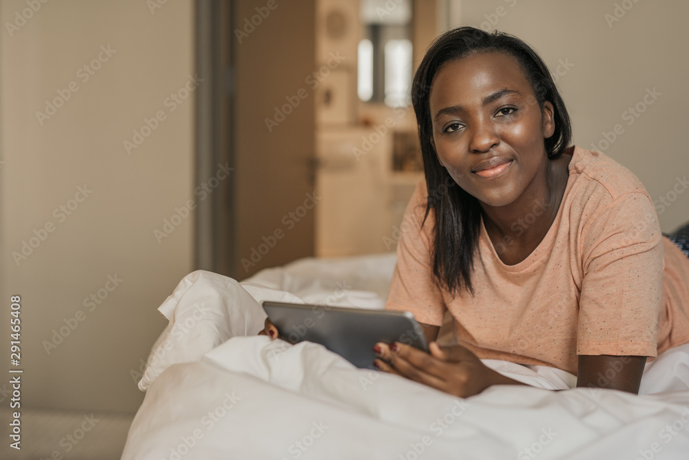 Smiling African American woman using a tablet on her bed Smiling African American woman using a tablet on her bed