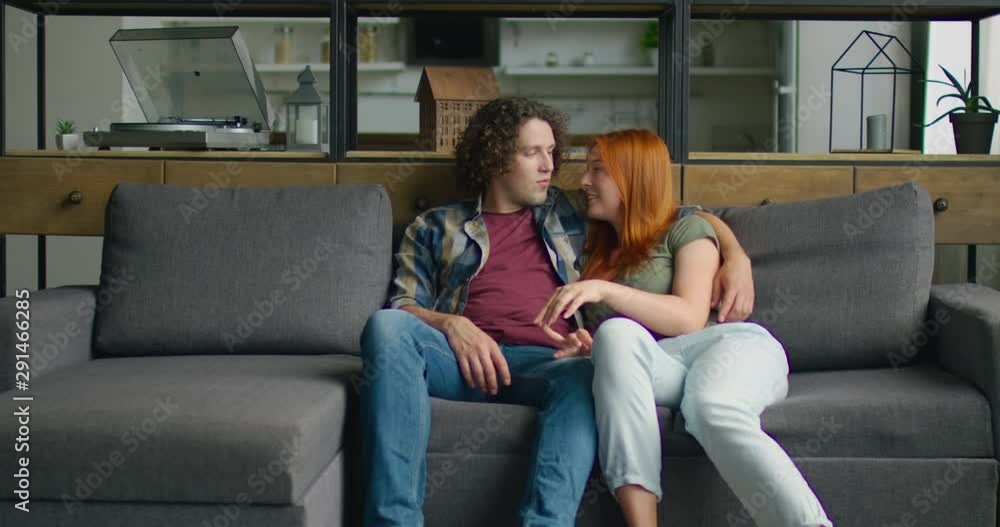 Young couple in love is relaxing on sofa at home, smiling, hugging, celebrating their love, enjoying their relationships, Caucasian. 4K, Middle plan, shot on RED camera. Young couple in love is relaxing on sofa at home, smiling, hugging, celebrating their love, enjoying their relationships, Caucasian. 4K, Middle plan, shot on RED camera.