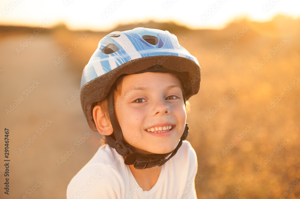 portrait of happy smiling cute little caucasian boy in blue sport helmet and white shirt on summer warm sunset outdoors portrait of happy smiling cute little caucasian boy in blue sport helmet and white shirt on summer warm sunset outdoors