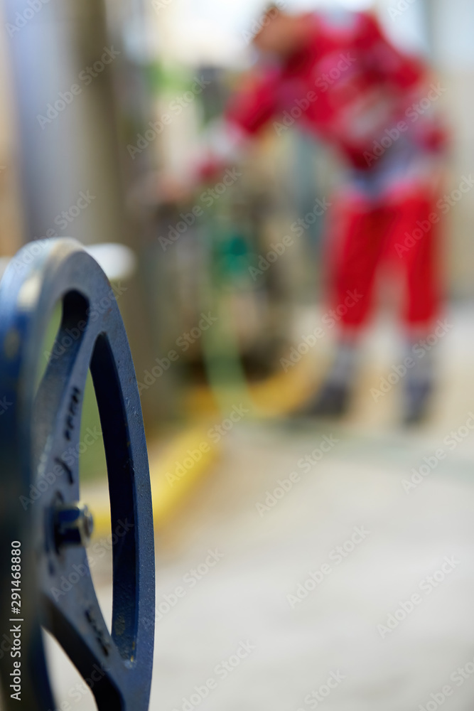Fototapeta premium Heating valve control wheel. Blurred background. A technician in red overalls is servicing heating technology. Start of hot water supply into big city heating network. Heating season coming.