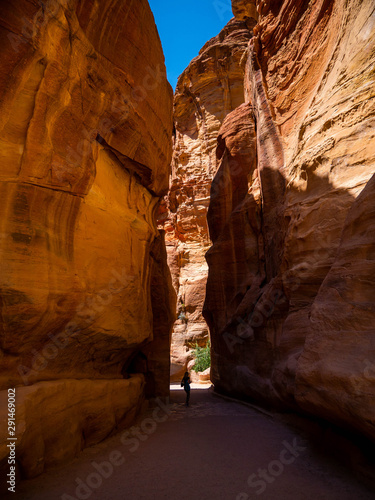 Steep cliffs of a canyon leading to the historical site of Petra, Jordan, light shining from blue sky on dark sandstone walls