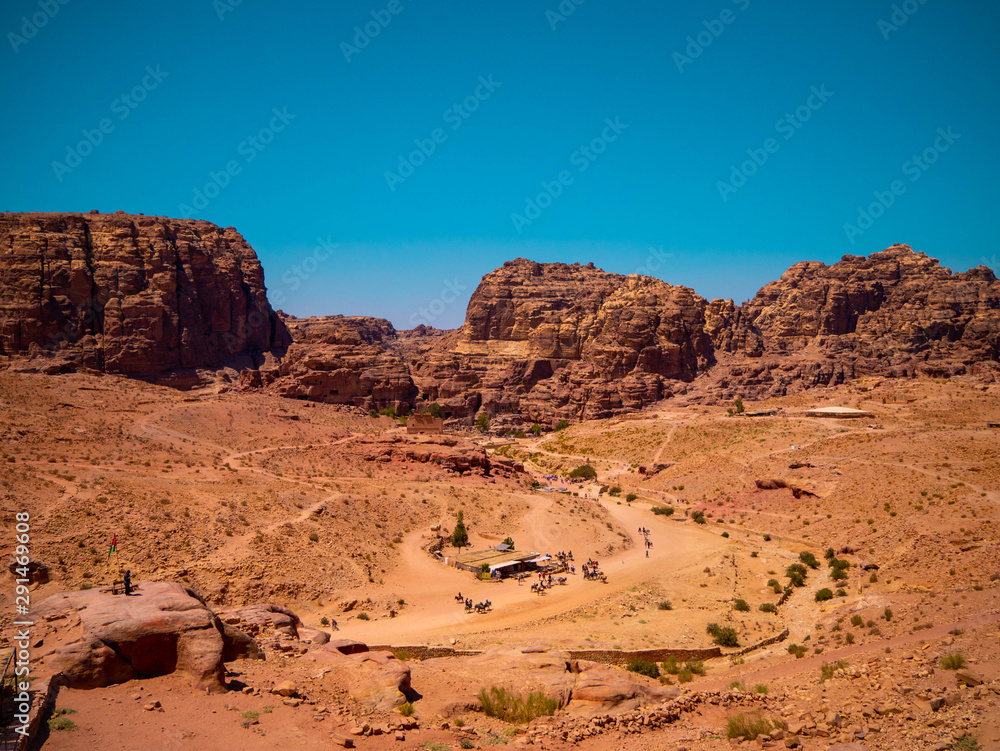 View of the valley of the historic site of Petra, Jordan, orange desert full of temples and a roman amphitheatre, seen from aerial perspective from a sandstone mountain View of the valley of the historic site of Petra, Jordan, orange desert full of temples and a roman amphitheatre, seen from aerial perspective from a sandstone mountain