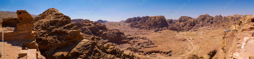 View of the valley of the historic site of Petra, Jordan, orange desert full of temples and a roman amphitheatre, seen from aerial perspective from a sandstone mountain