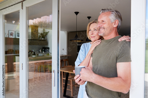 Bild auf Leinwand Senior Couple Standing And Looking Out Of Kitchen Door Drinking Coffee