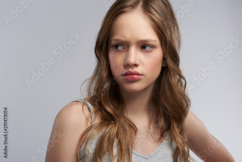 Upset teen girl standing against gray-white background