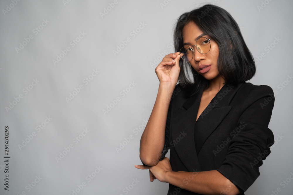 Portrait of attractive young Asian woman in elegant black blazer and glasses posing over light gray wall background. Mock up copy space Portrait of attractive young Asian woman in elegant black blazer and glasses posing over light gray wall background. Mock up copy space