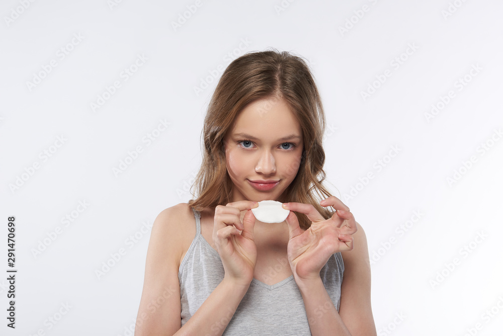 Charming teen girl in gray tank top holding cotton pad Charming teen girl in gray tank top holding cotton pad