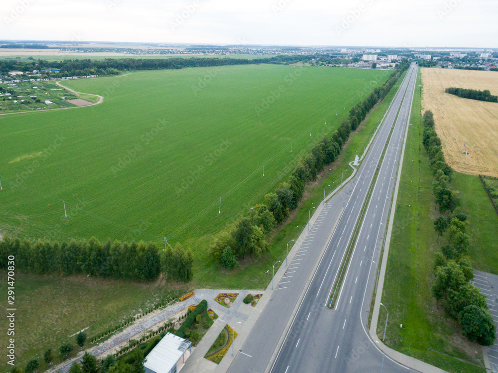 Top view asphalt road, highway, a crossroads in the village on a bright sunny day. Aerial photo with green forest, grass