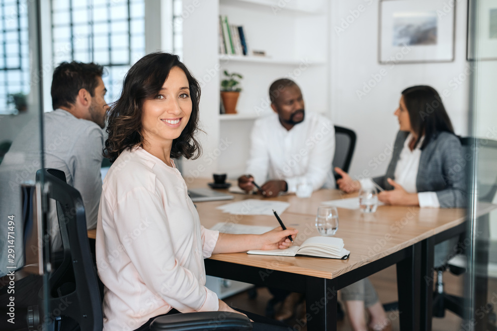 Smiling young businesswoman sitting with coworkers during a meeting Smiling young businesswoman sitting with coworkers during a meeting