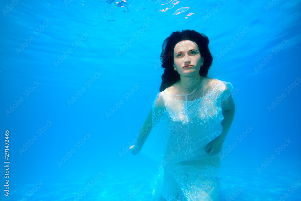 Beautiful bride in white dress posing underwater at the bottom of the pool on a Sunny day. Unusual wedding. Fashion portrait.