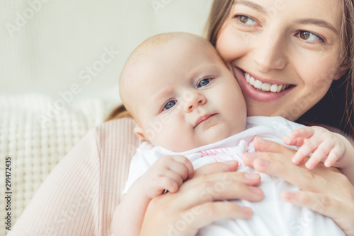 attractive and smiling mother holding her child in apartment