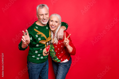 Photo of two elderly positive cheerful carefree excited partners enjoying x-mas tradition having good mood showing v-sign waiting for eve noel santa claus isolated bright color background