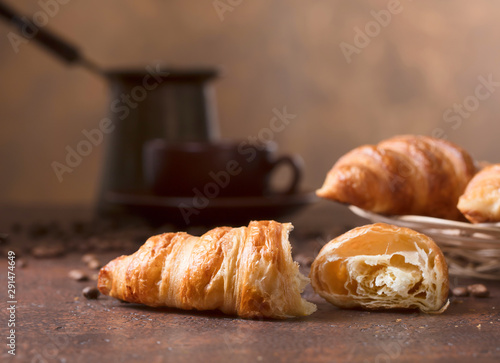 Fresh and tasty croissant  and cup of coffee on old copper background.