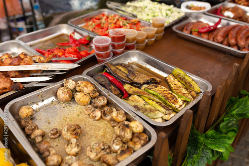 A counter with metal trays containing grilled food. Food and cooking equipment at a street food festival