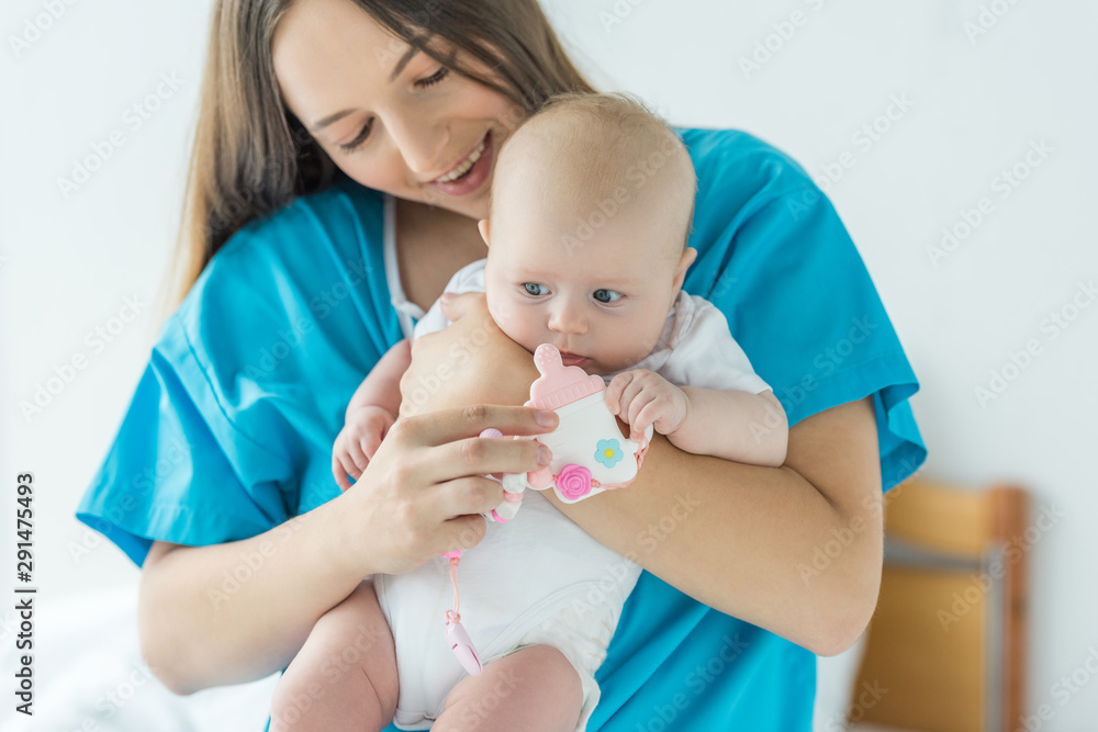 attractive and smiling mother holding her child with toy in hospital attractive and smiling mother holding her child with toy in hospital