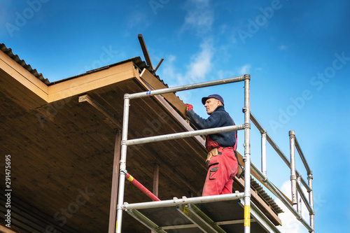 old house renovation - construction worker installing new planks on house roof eaves