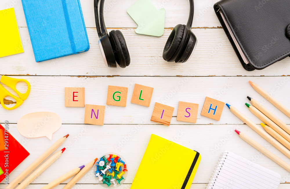 Top view desktop with notebooks, earphones and English word made from wooden cubes. Learning language concept Top view desktop with notebooks, earphones and English word made from wooden cubes. Learning language concept