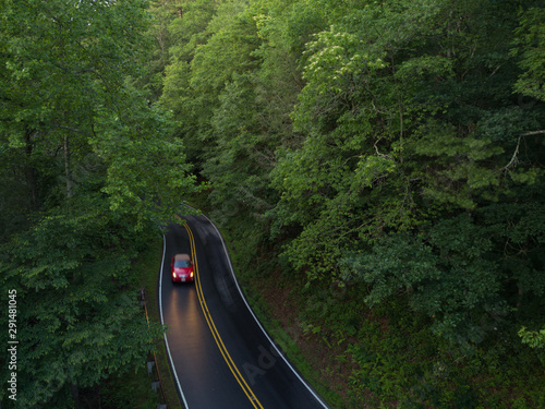 An aerial view of a red car driving down a wet winding road just after a rain storm.