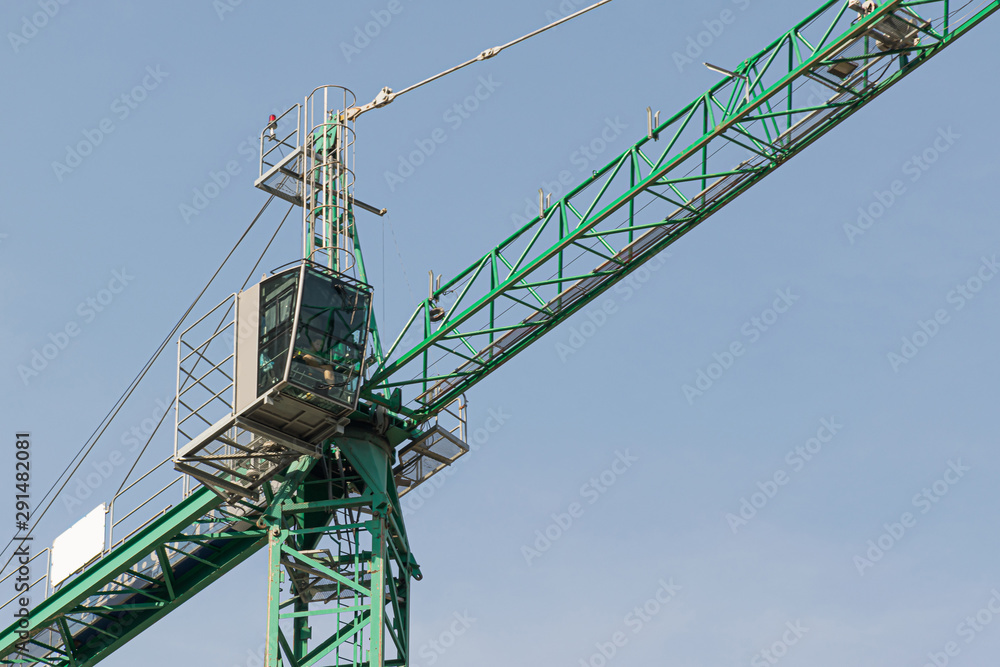 A high-rise construction crane against the blue sky builds multi-storey residential buildings using modern technologies of metal, concrete and brick according to the architectural design