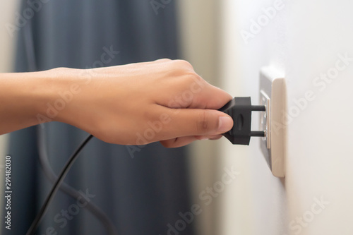 hand insetring, plugging or unplugging eclectrical wall outlet; concept of energy usage, consumption or power saving