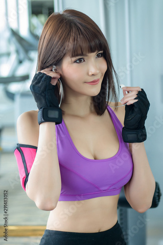 Fototapeta Naklejka Na Ścianę i Meble -  healthy strong fitness woman working out in gym with music headphone. portrait of fitness woman in gym posing for strong body, gym workout, fitness people, healthy lifestyle concept. asian woman mode