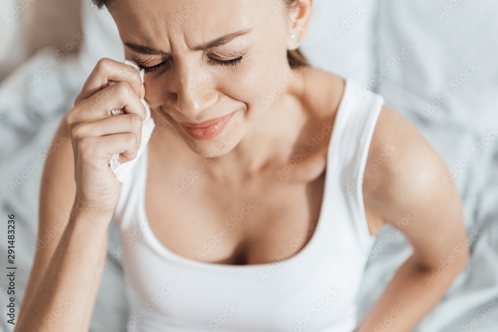 stressed young woman crying and wiping tears with napkin