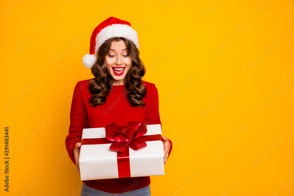 Pretty lady holding large giftbox in arms wear knitted pullover and santa hat isolated yellow background