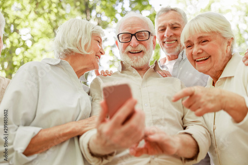 Cheerful elderly people using modern cellphone outdoors