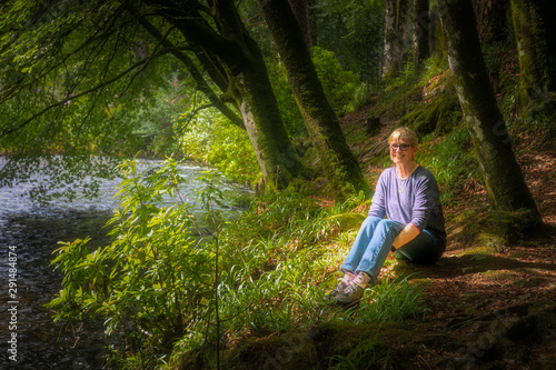 Woman sitting on the ground next to a stream in Glencoe, Scotland.