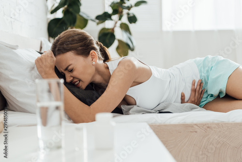 suffering woman in bed and pills with glass of water on foreground
