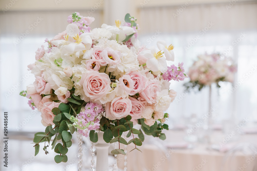 Large wedding flowers, white and cream roses, eucalyptus leaves decorate the banquet hall of the restaurant