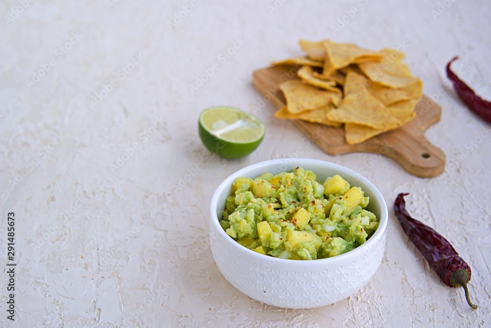 Appetizer, guacamole with mango in a white bowl on a light concrete background. Served with corn chips nachos. Mexican cuisine. Copy space. Appetizer, guacamole with mango in a white bowl on a light concrete background. Served with corn chips nachos. Mexican cuisine. Copy space.