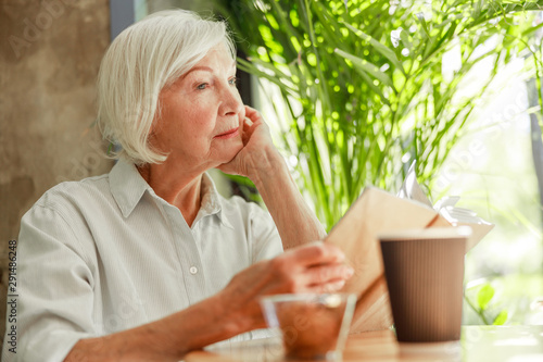 Tableau sur toile Pensive old woman reading book at outdoor cafe
