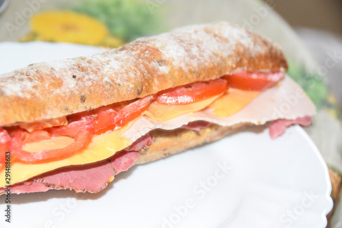 Sandwich in a baguette with ham, cheese, chicken and tomato