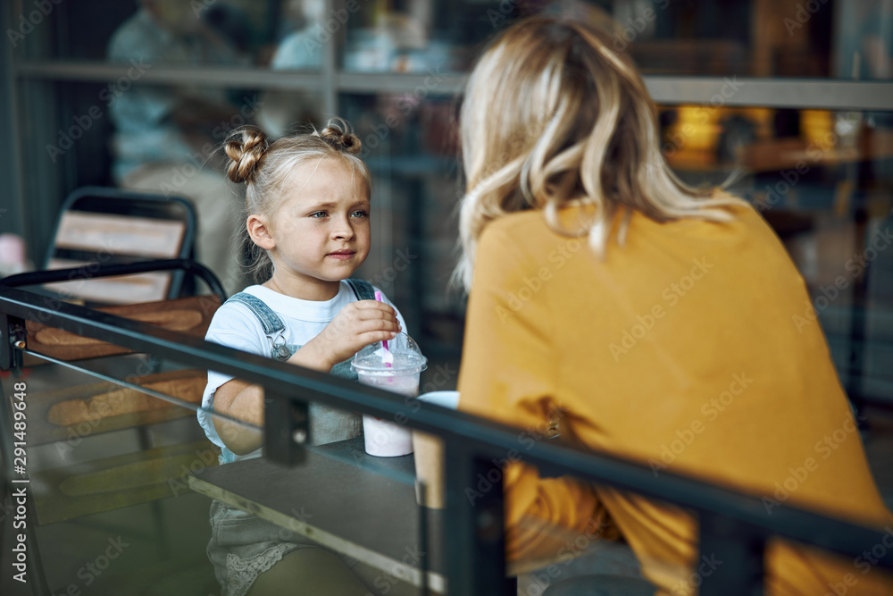 Girl drinking milkshake and looking at mother stock photo