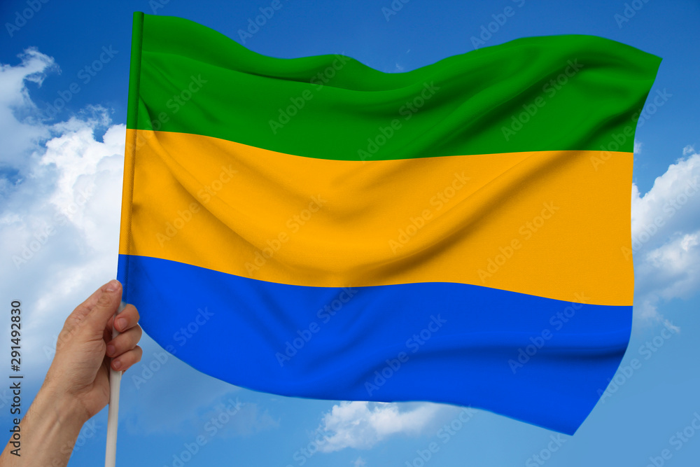 hand holds against the background of the sky with clouds the color flag of Gabon on the texture of the fabric, silk with waves, close-up hand holds against the background of the sky with clouds the color flag of Gabon on the texture of the fabric, silk with waves, close-up