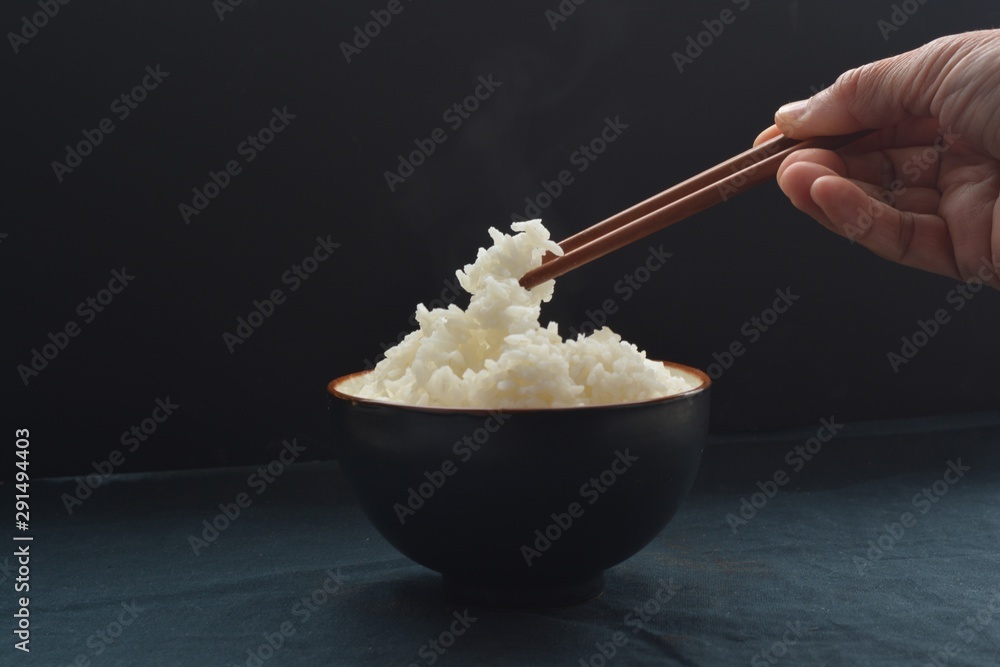 A small bowl of rice with chopsticks grabbing the rice in front of a black background A small bowl of rice with chopsticks grabbing the rice in front of a black background
