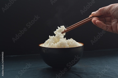 A small bowl of rice with chopsticks grabbing the rice in front of a black background